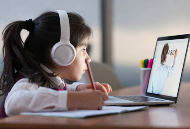 Little girl attending to online school class on laptop computer