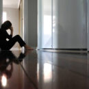 Sad adult woman sitting on dark home corridor floor