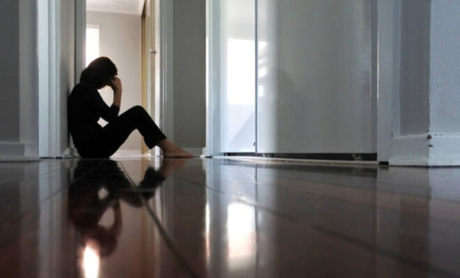 Sad adult woman sitting on dark home corridor floor
