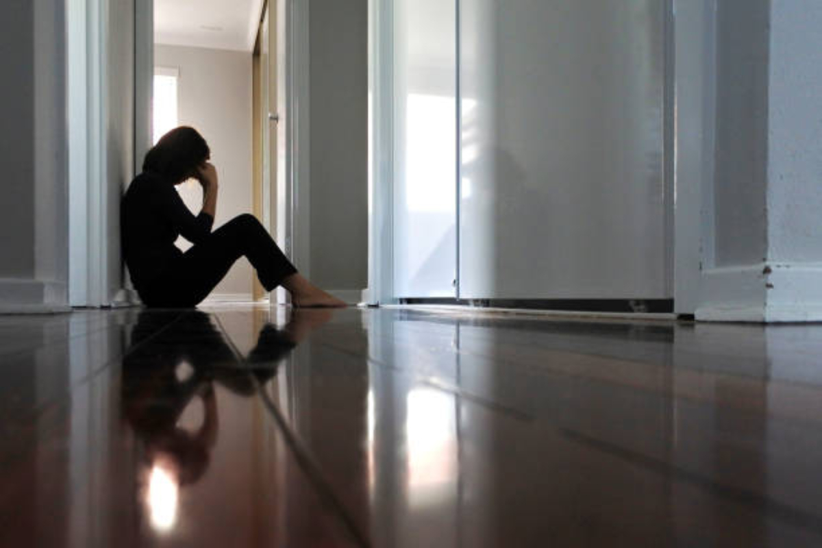 Sad adult woman sitting on dark home corridor floor