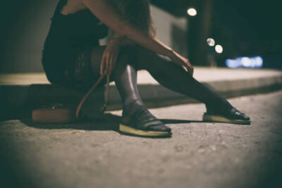 Drunk woman in dress sits on the roadside at night.