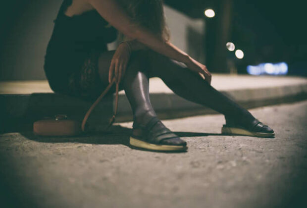 Drunk woman in dress sits on the roadside at night.