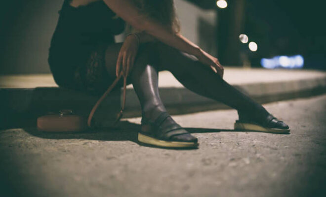 Drunk woman in dress sits on the roadside at night.