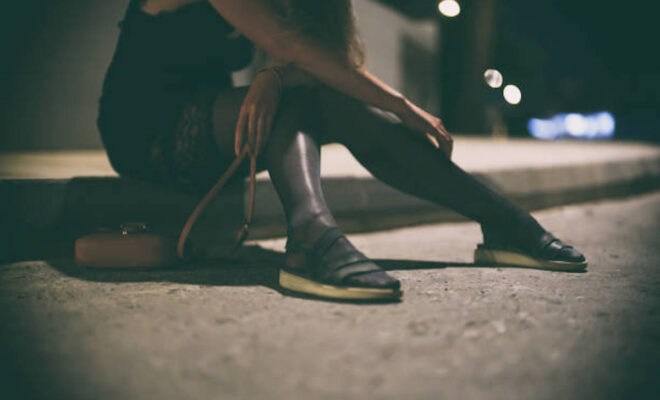 Drunk Woman In Dress Sits On The Roadside At Night.