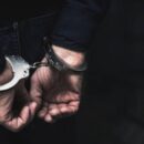 Handcuffed arrested man behind prison bars. copy spac