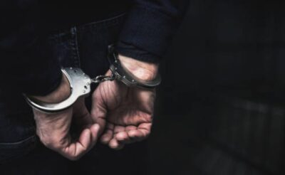 Handcuffed arrested man behind prison bars. copy spac