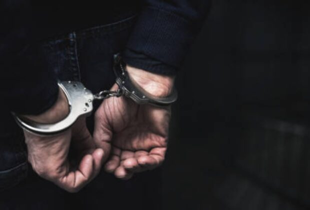 Handcuffed arrested man behind prison bars. copy spac