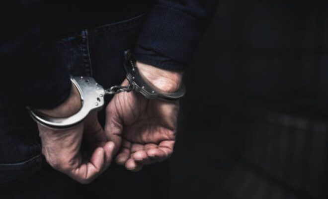 Handcuffed arrested man behind prison bars. copy spac