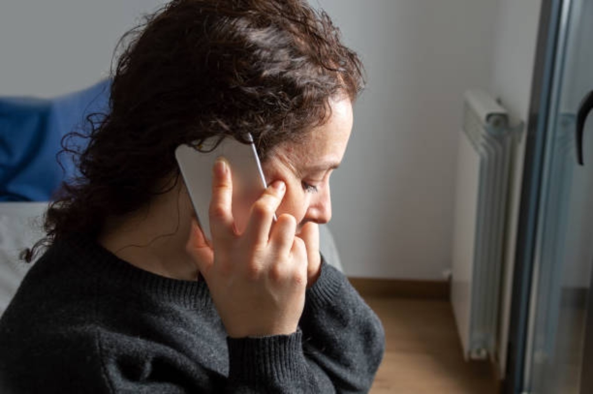 Close Up Of Serious Woman Attending A Phone Call Sitting On A Bed In The Bedroo