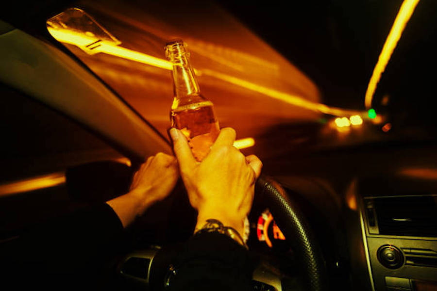 Car Driver Holds An Alcholic Beverage While Driving At Night